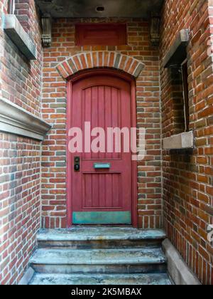 Porte rouge dans un renfoncement à l'arrière d'un bâtiment en brique Banque D'Images