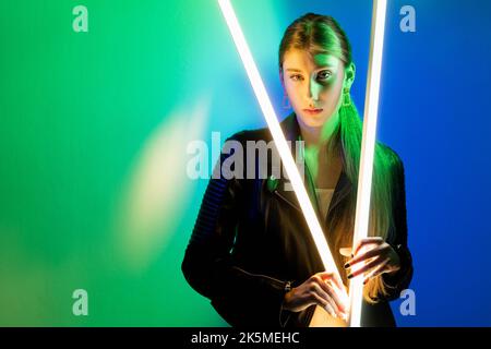 Lumière de néon personnes. La beauté du cyberpunk. Portrait futuriste. Vert bleu phosphorescent confient fille dans une veste en cuir noir avec lampe LED isolée sur le soupir Banque D'Images