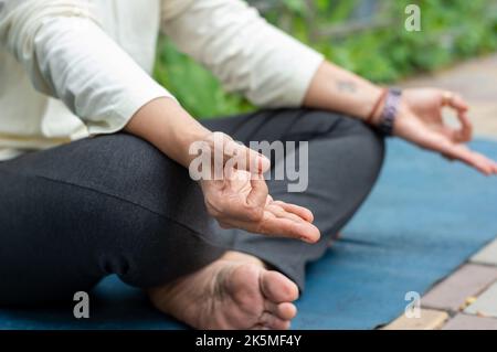 Gros plan femme mudra main geste faisant yoga détente en position lotus assis sur le tapis. À l'extérieur. Pratiquer la méditation dans la nature. Photo d'arrière-plan. Banque D'Images