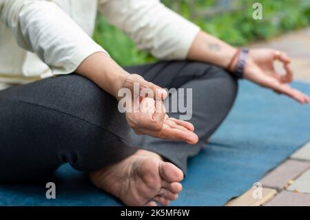 Gros plan femme mudra main geste faisant yoga détente en position lotus assis sur le tapis. À l'extérieur. Pratiquer la méditation dans la nature. Photo d'arrière-plan. Banque D'Images