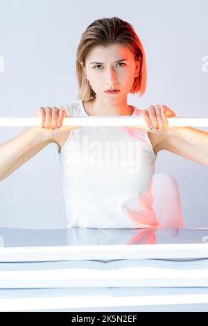 Visage insatisfait. Portrait clair en couleur. Émotion négative. Lumière au néon rouge agacé malheureux femme offended avec lampe LED blanche isolée sur neutre. Banque D'Images