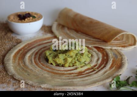 Kodo millet masala dosa. Fines crêpes croustillantes faites de farine de millet kodo et de lentilles, farcies de purée de pommes de terre épicée. Prise de vue sur fond blanc. Banque D'Images