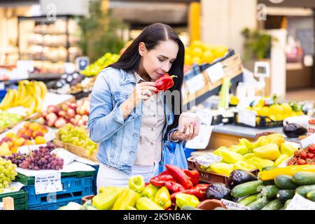 Le wman Brunette sent le poivre rouge de la sélection colorée de fruits et légumes sur le marché agricole. Banque D'Images