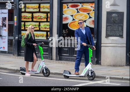 LONDRES - 21 mai 2022: Homme et femme bien habillés sur la location de scooters électriques Banque D'Images