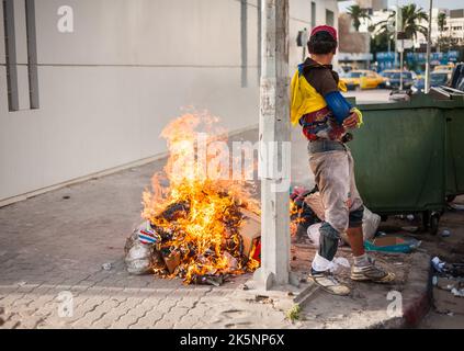 Sousse, Tunisie-09/17/2019: Rue de la ville, Sousse. Un résident local dans des vêtements sales dansant près du feu, près des ordures. Attirer l'attention sur hi Banque D'Images