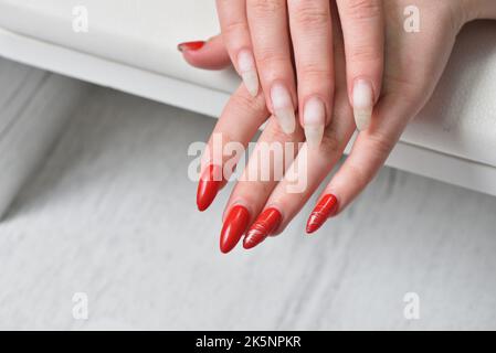 Les mains des femmes avec des ongles rouges en gel renoyés gros plan. Banque D'Images