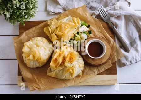 Porte-monnaie phyllo. Pâte filo remplie de poulet et de légumes sur papier parchemin et sauce barbecue. Trois sachets de pâtisseries veggie fourrées au four. Vege mixte Banque D'Images