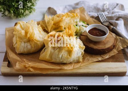 Porte-monnaie phyllo. Pâte filo remplie de poulet et de légumes sur papier parchemin et sauce barbecue. Trois sachets de pâtisseries veggie fourrées au four. Vege mixte Banque D'Images