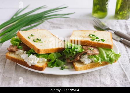 Deux croque-monsieur avec sauce à la crème, bacon et feuilles de laitue bouclés. Garni d'oignons verts frais. Un petit déjeuner appétissant. Banque D'Images