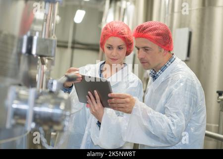 les travailleurs de la brasserie portant des filets à cheveux regardant l'écran d'une tablette Banque D'Images