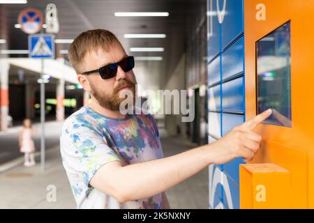 L'homme saisit le code de colis à l'écran et récupère le colis à partir de la machine postale automatisée. Man tient son smartphone à l'aide d'un terminal de messagerie automatique en libre-service cl Banque D'Images