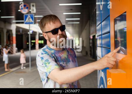 L'homme saisit le code de colis à l'écran et récupère le colis à partir de la machine postale automatisée. Man tient son smartphone à l'aide d'un terminal de messagerie automatique en libre-service cl Banque D'Images