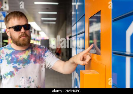 L'homme saisit le code de colis à l'écran et récupère le colis à partir de la machine postale automatisée. Man tient son smartphone à l'aide d'un terminal de messagerie automatique en libre-service cl Banque D'Images