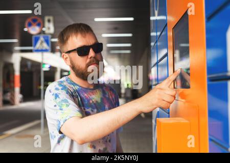 L'homme saisit le code de colis à l'écran et récupère le colis à partir de la machine postale automatisée. Man tient son smartphone à l'aide d'un terminal de messagerie automatique en libre-service cl Banque D'Images