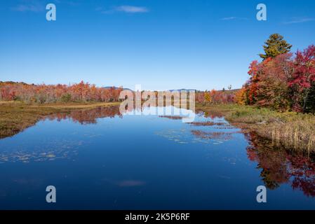 Feuillage d'automne et ciel bleu se reflétant sur le point de sortie du lac Sacandaga à Lake Pleasant, NY USA dans les montagnes Adirondack. Banque D'Images