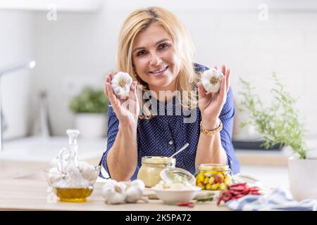 La femme tient des têtes d'ail dans ses mains tandis que divers types de conserves d'ail l'entourent. Banque D'Images