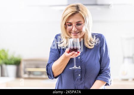 Une femme souriante sent le vin rouge versé dans le verre à la maison. Banque D'Images