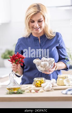 Femme tenant un bol d'ail frais et de piments faisant des conserves dans la cuisine. Banque D'Images