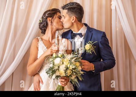 Les jeunes mariés ont leur premier baiser avec du champagne entre leurs mains. Banque D'Images