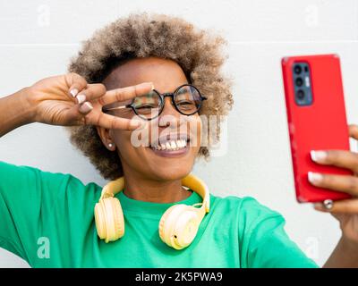 Jeune femme afro-américaine souriante avec cheveux afro et casque prenant un selfie Banque D'Images