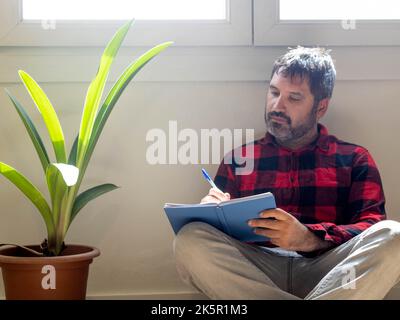 Hipster homme écrivant dans un carnet dans un appartement Banque D'Images