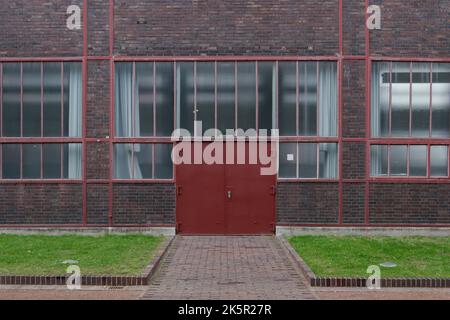 Gros plan de la façade de l'ancien bâtiment industriel ou d'usine avec un mur en brique rouge rugueux, des fenêtres en verre et un cadre et une porte en acier rouge. Banque D'Images