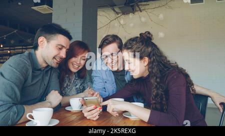 Les jeunes gens heureux regardent l'écran du smartphone discuter des photos et rire pendant la pause déjeuner dans le café. Amitié, technologie moderne et concept de style de vie moderne. Banque D'Images