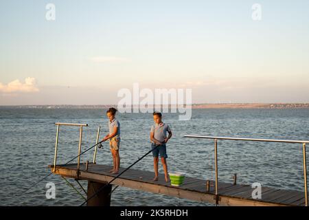 Les petits garçons pêchent au coucher du soleil sur le lac. Loisirs et loisirs d'été Banque D'Images