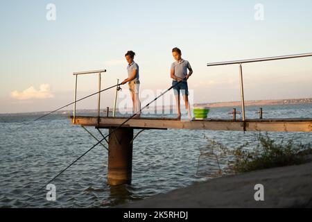 Les petits garçons pêchent au coucher du soleil sur le lac. Loisirs et loisirs d'été Banque D'Images