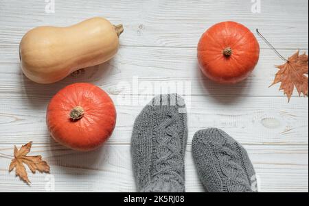 Pattes d'une fille en chaussettes tricotées sur fond de bois à côté de citrouilles et de feuilles d'automne. Concept d'automne confortable. Banque D'Images