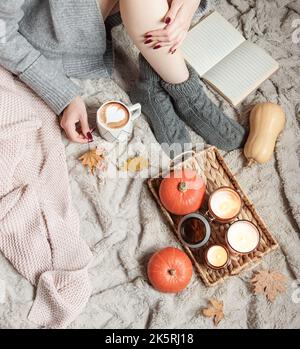 Une fille dans un chandail et des chaussettes tricotées se trouve sur une couverture. Concept d'automne confortable. Citrouilles et bougies sur un plateau près de la fille. Banque D'Images