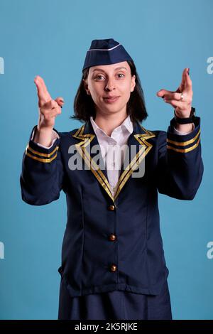 Préposé de vol souriant montrant la sortie de secours à bord de l'avion, démonstration des consignes de sécurité. Hôtesse en uniforme professionnel pointant avec les doigts sur la vue avant de la caméra Banque D'Images