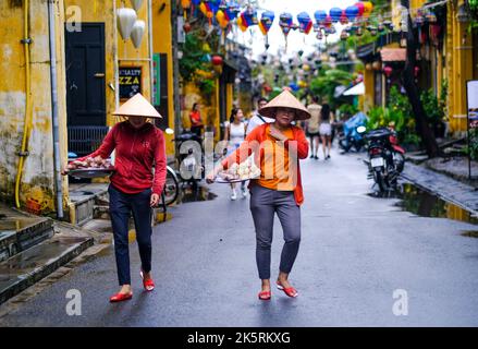 Deux vendeurs d'aliments vietnamiens marchent le long de la route dans la vieille ville de Hoi an, Vietnam. Banque D'Images