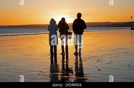 Portobello, Édimbourg, Écosse, Royaume-Uni. 10th octobre 2022. Lever de soleil frais à 9 degrés centigrade pour ceux qui s'aventurer en bord de mer par Firth of Forth pour faire de l'exercice ou tout simplement s'imprégner de la lumière de l'aube. En photo : trois touristes qui se reflètent dans la pluie admirent la couleur de l'aube. Crédit : Arch White/alamy Live News. Banque D'Images