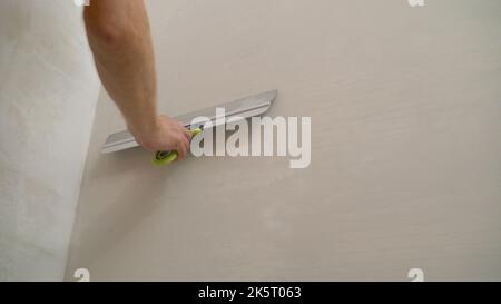 L'ouvrier crache les murs à l'aide d'une spatule. Spatule avec mastic à la main. Le travailleur met du plâtre sur le mur. Banque D'Images