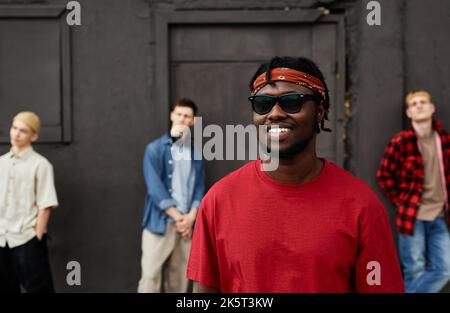 Divers groupes de garçons portant des vêtements de rue debout contre le mur noir à l'extérieur et regardant l'appareil photo, se concentrent sur l'homme afro-américain souriant Banque D'Images