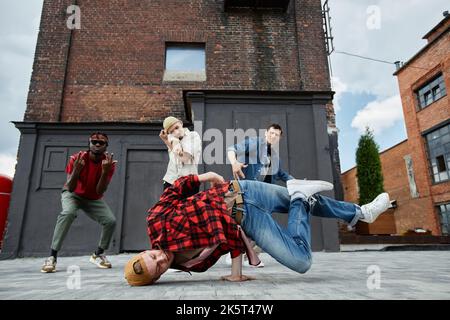 Prise de mouvement d'un jeune homme faisant de la breakdance pose à l'extérieur avec toute l'équipe de danse masculine en arrière-plan Banque D'Images