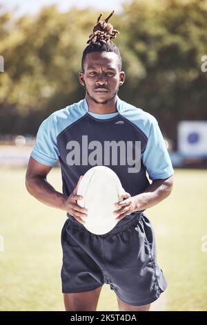 Portrait d'un jeune joueur de rugby afro-américain tenant un ballon de rugby tout en se tenant sur le terrain. Homme noir plein de confiance et prêt à l'emploi Banque D'Images