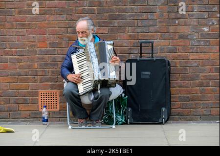 LONDRES - 21 mai 2022 : un busseur âgé avec une barbe blanche joue de l'accordéon à côté du vieux mur de briques rouges Banque D'Images