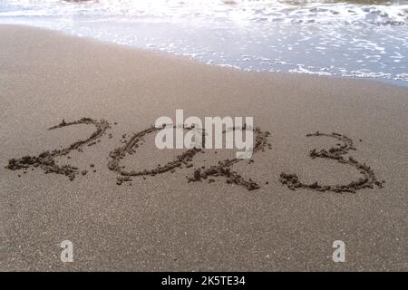 Texte bonne année 2023 sur une plage de sable avec une petite vague. Résumé photo de fond du nouvel an 2023 à venir Banque D'Images