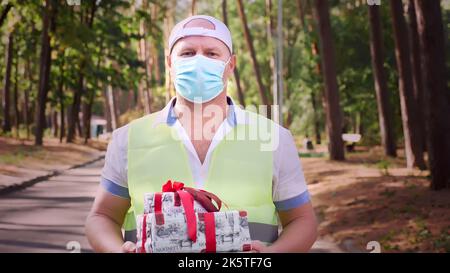 cadeaux emballés. homme, coursier, dans un masque de protection, tenant plusieurs boîtes magnifiquement emballées dans ses mains. extérieur. livraison de cadeaux pour une fête. don, concept de charité. Photo de haute qualité Banque D'Images