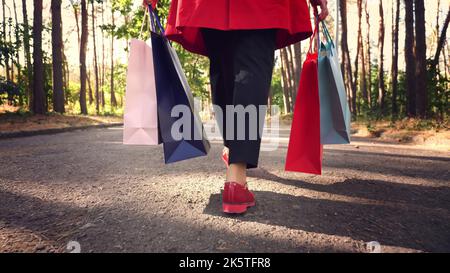femme avec sacs de shopping. jambes de femme en chaussures rouges, gros plan. Femme avec des sacs de shopping colorés dans ses mains, marchant dans le parc de la ville. Shopping et cadeaux. Livraison ou don concept. Photo de haute qualité Banque D'Images