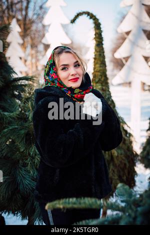 Belle fille dans un foulard et des moufles blanches en hiver parmi les arbres de Noël Banque D'Images