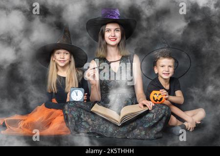 Une famille heureuse en costumes de sorcières et de sorciers, tenant un grand livre avec des prédictions, des paniers en forme de citrouille, une montre noire et un Banque D'Images