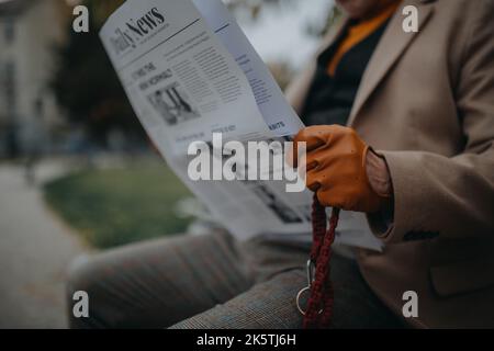 Homme senior assis sur le banc et lisant le journal à l'extérieur dans le parc de la ville. Banque D'Images