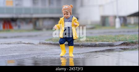 Joyeux petit garçon sautant dans la flaque après la pluie en automne. Banque D'Images