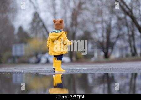 Joyeux petit garçon sautant dans la flaque après la pluie en automne. Banque D'Images