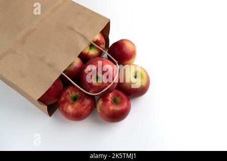 pommes rouges mûres juteuses versées dans un sac en papier isolé sur fond blanc, fruits frais biologiques gros plan avec espace vide pour le texte Banque D'Images