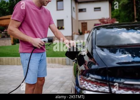 Homme tenant le câble d'alimentation électrique à la station de charge du véhicule électrique. Banque D'Images