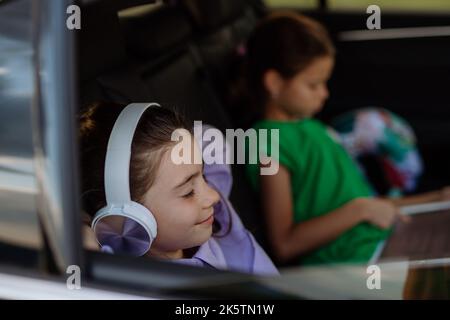 Petites sœurs assises en voiture, écoutant de la musique et attendant un voyage en voiture. Banque D'Images